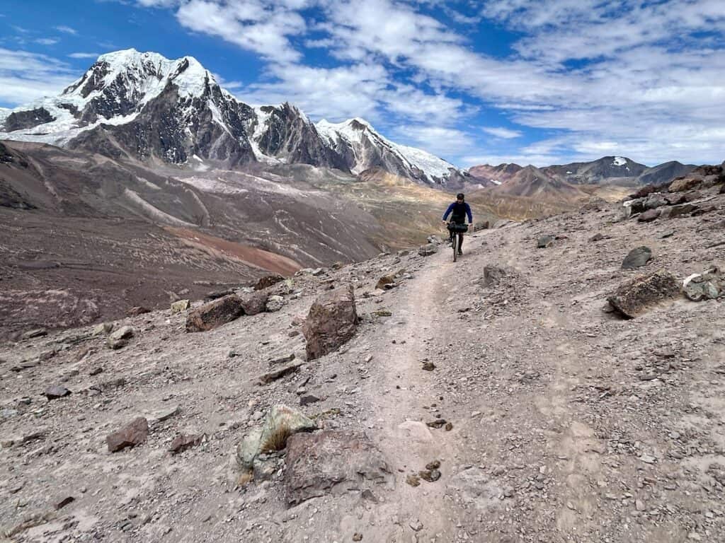 Bikepacker riding bike on trail with snow-capped mountain in the background