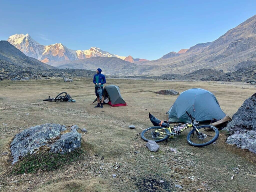 Bikepacker setting up tents on remote plain at the base of snow-capped mountains in Peru