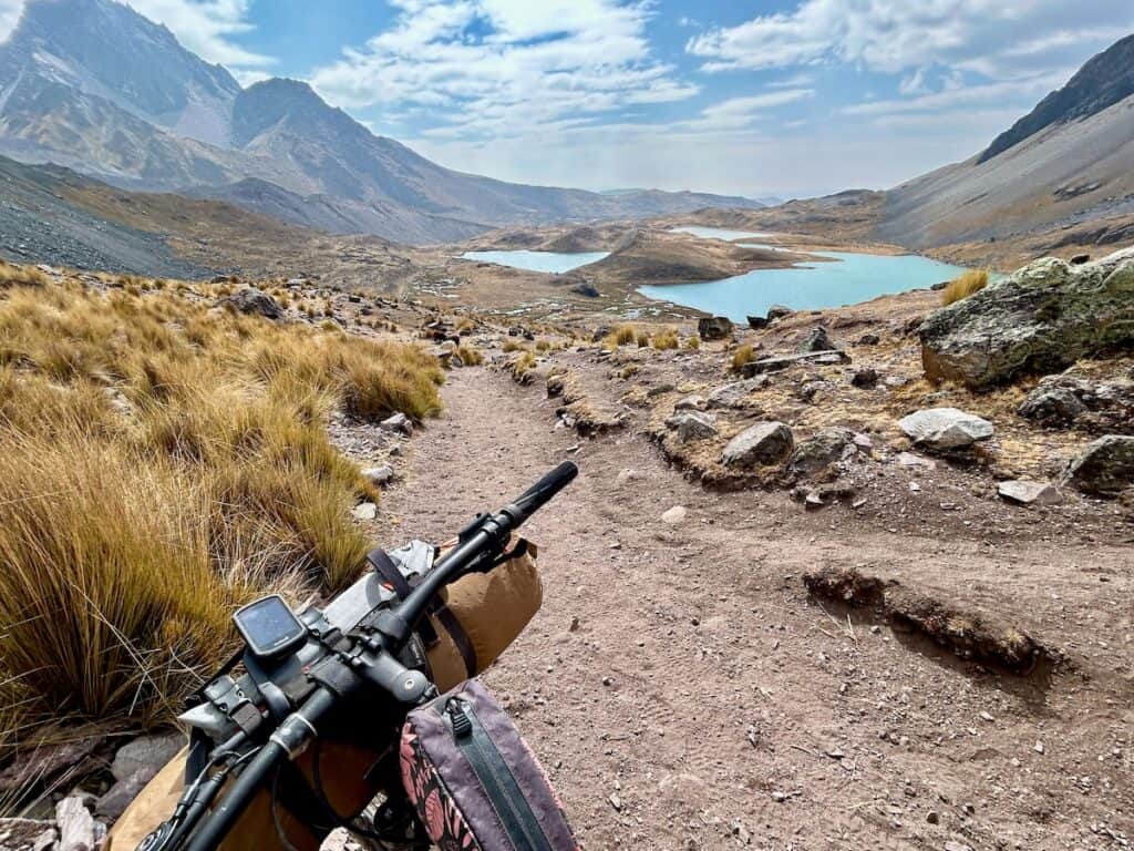 Photo out over front of bikepacking bike onto turquoise alpine lakes and Peruvian Andes landscape