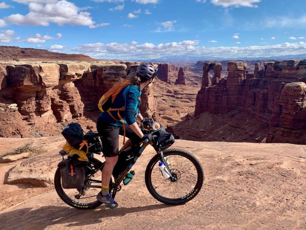 Bikepacker riding loaded bike while looking out over incredible canyonland views from the White Rim Trail