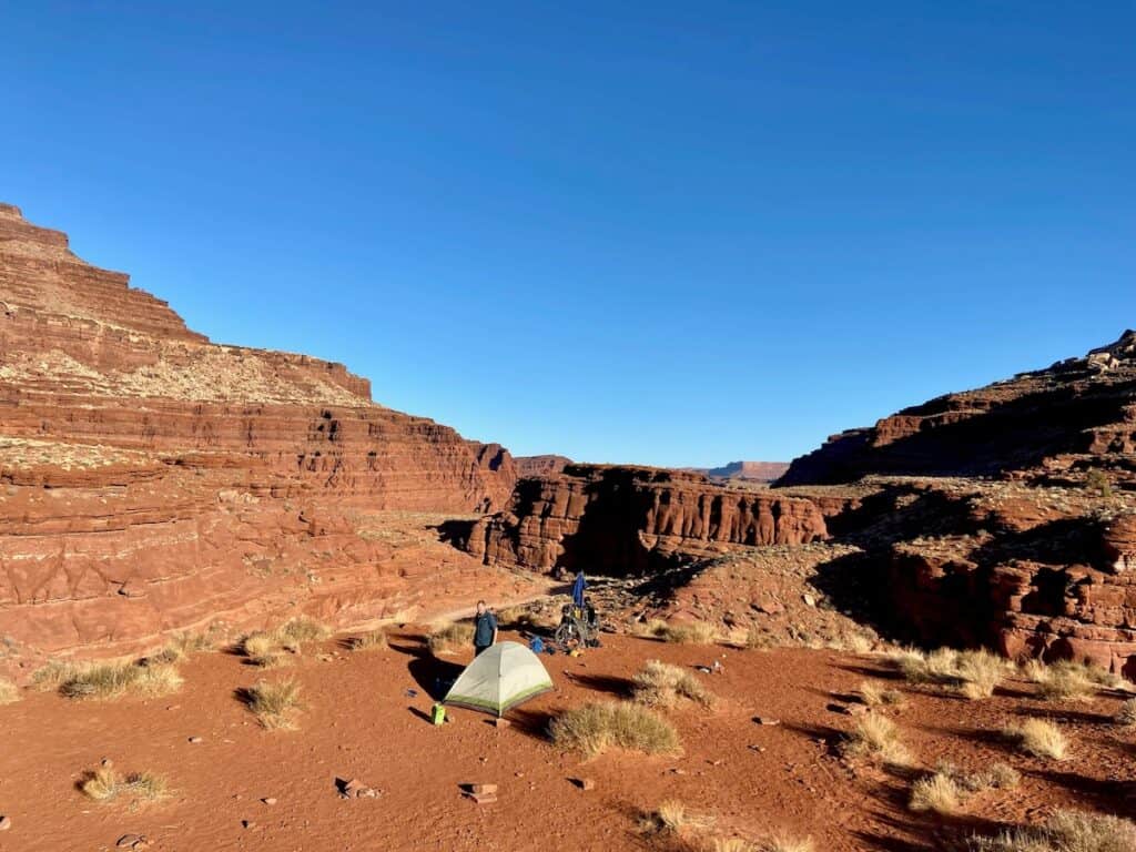 Tent set up at remote campground surrounded by red dirt and red rocks in Utah