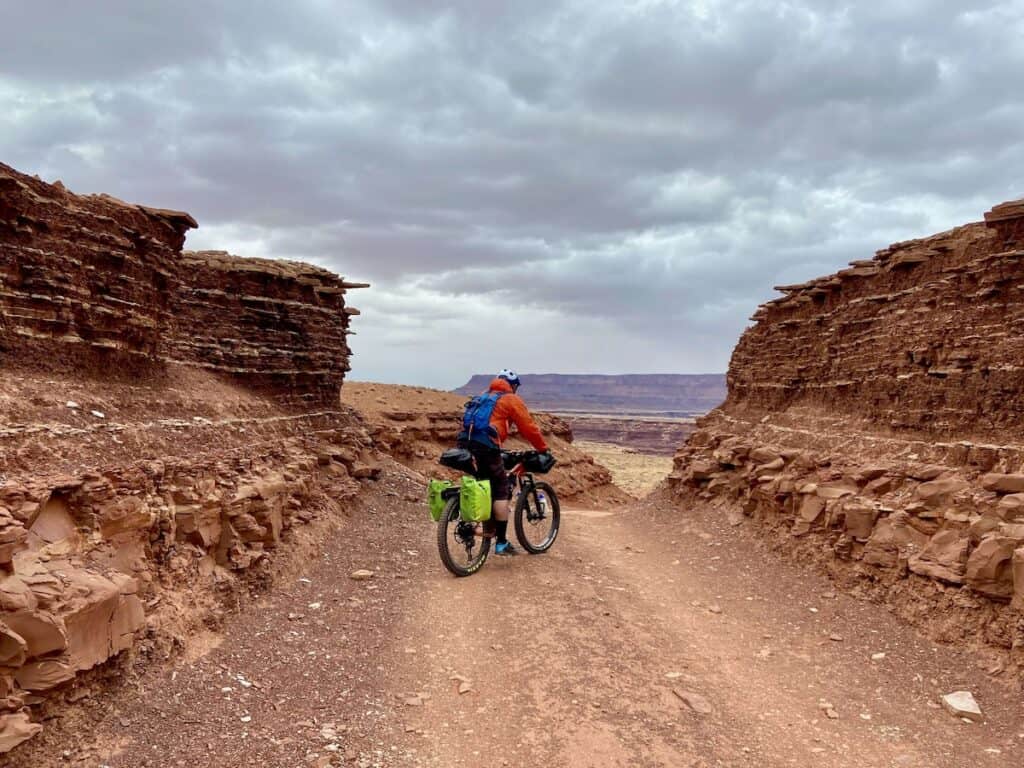 Man riding loaded bikepacking bike on remote red dirt road surrounded by by Utah canyonland views