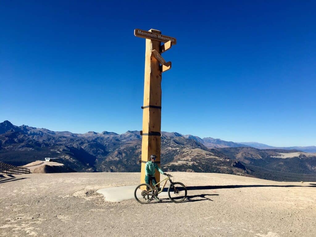 Mountain biker standing under tall wooden sign at the summit of Mammoth Mountain Bike Park