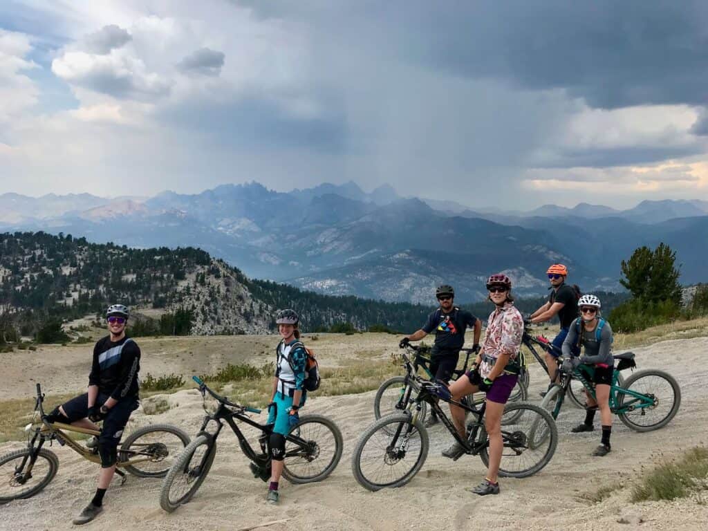 Group of mountain bikers stopped on trail for photo with stormy skies and stunning mountain landscape behind them