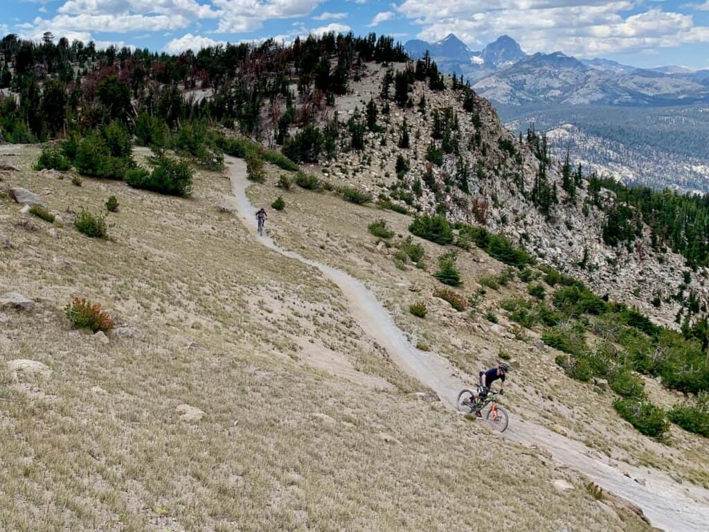 Two mountain bikers riding down flowy section of singletrack at Mammoth Bike Park in California with Sierra Mountains in distance