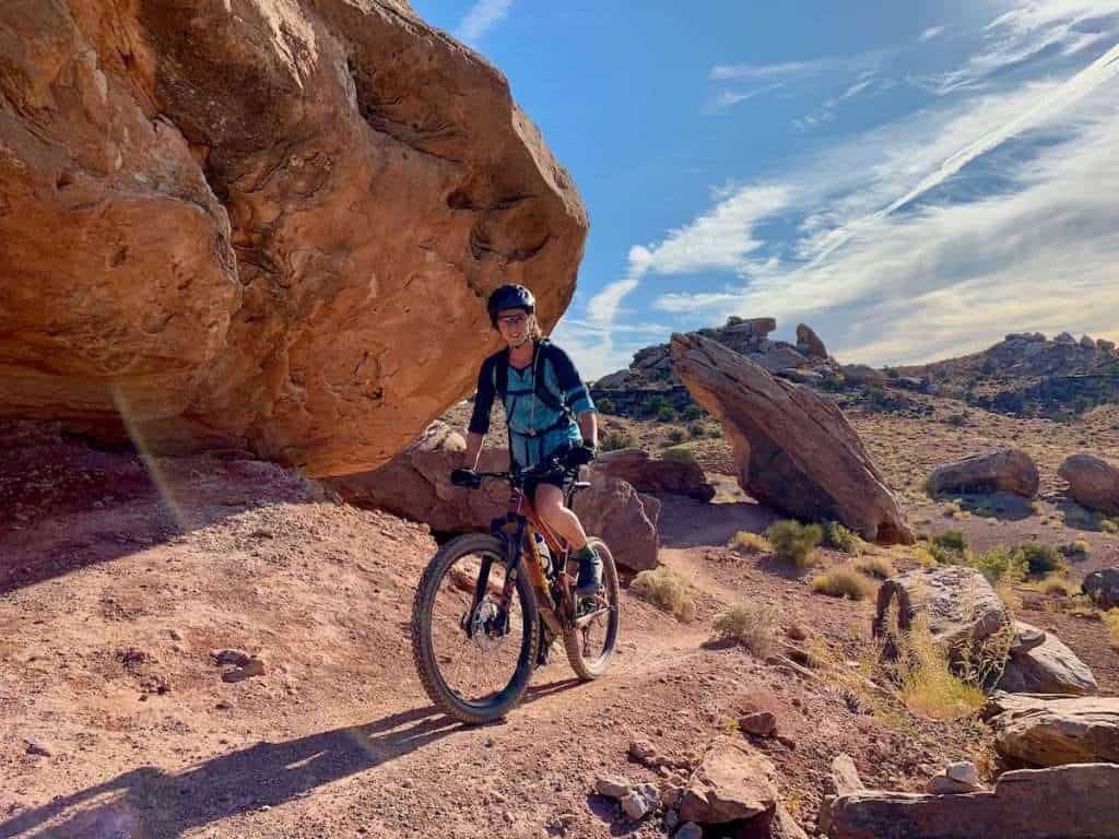 Becky riding mountain bike on singletrack trail in Moab, Utah with tall boulders lining the trail