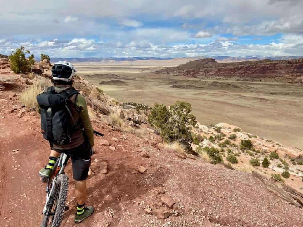 Mountain biker facing away from camera looking out over desert landscape from atop a bluff in Moab, Utah