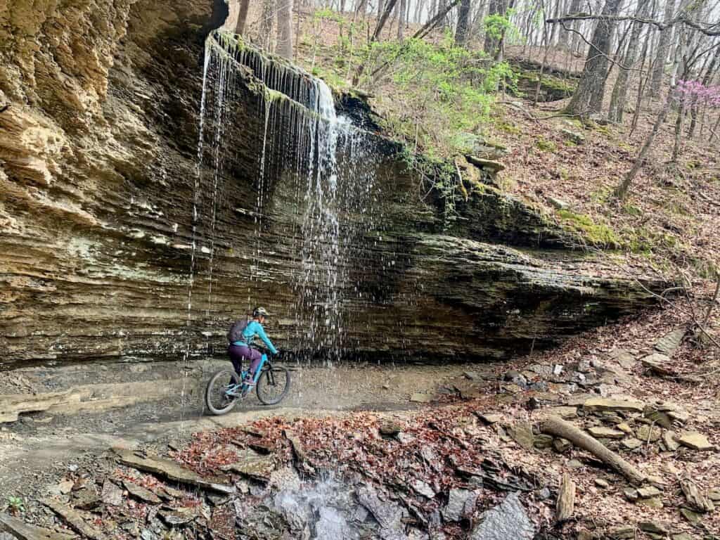 Mountain biker riding under waterfall at Devil's Den State Park in Arkansas