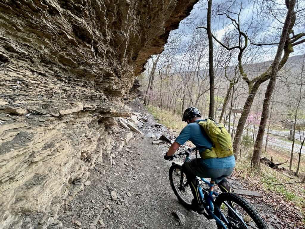 Mountain bike wearing Osprey Raptor hydration pack on trail underneath rock overhang in Arkansas