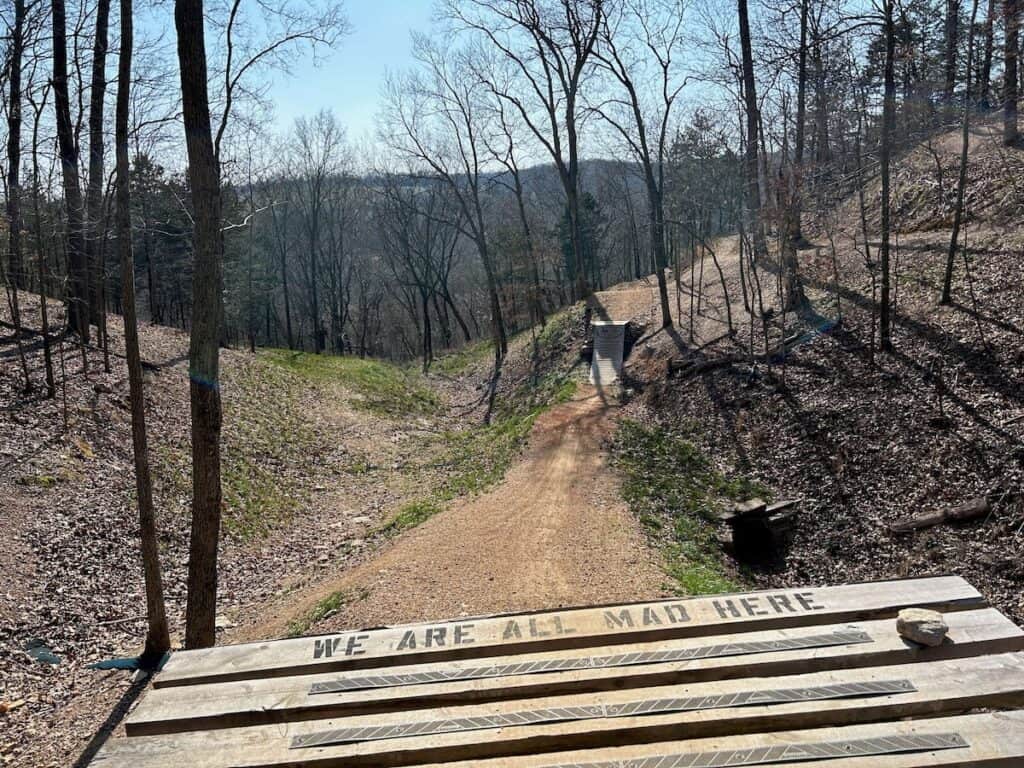 Wooden drop on mountain bike trail in Bentonville, Arkansas with "we are all mad" written on the edge