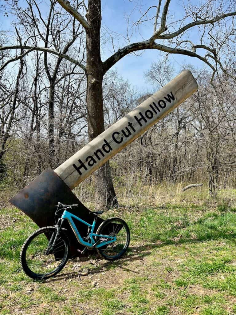 Mountain bike resting against giant Axe sculpture with "Hand Cut Hollow" written on handle