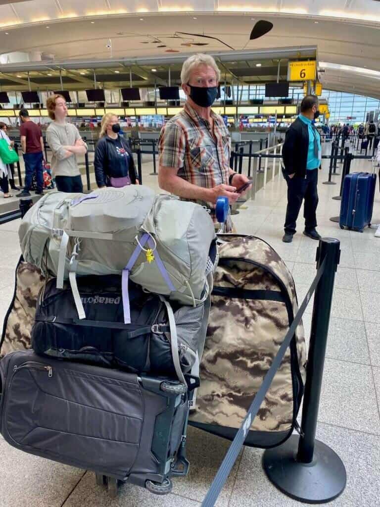 Man standing in line at airport next to car loaded with luggage and a bike travel bag