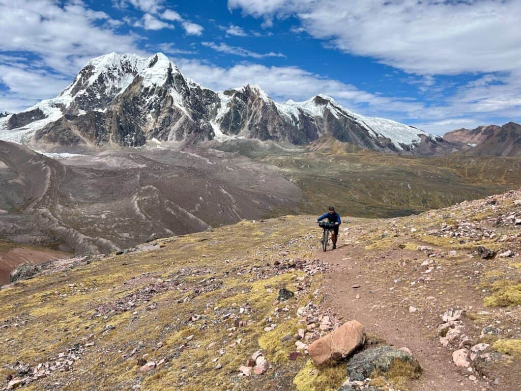 Bikepacker pushing bike up trail on the Ausangate Circuit in Peru with snow-capped mountain in the background